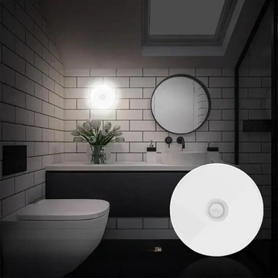 Salle de bain moderne avec lavabo, miroir rond, carrelage blanc, et lumière LED murale. Décor élégant et minimaliste.