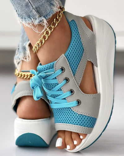 Chaussures de sport bleu et gris pour femme avec semelle compensée blanche, lacets bleus, et bracelet doré, portées avec un jean déchiré.