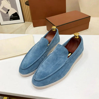 Mocassins en daim bleu pour homme sur une table blanche, boîte marron en arrière-plan. Chaussures élégantes, mode masculine, style décontracté.
