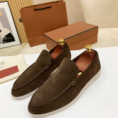 Mocassins en daim marron pour homme avec embauchoirs dorés, posés devant des boîtes en carton. Chaussures élégantes et modernes pour un style décontracté.