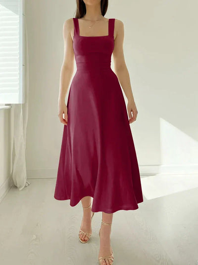 Robe longue bordeaux élégante, sans manches, avec bretelles larges, portée par une femme debout dans une pièce lumineuse. Mode féminine chic.