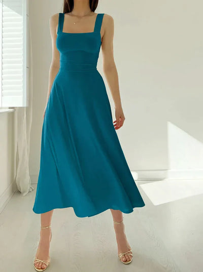 Robe longue bleue élégante sans manches, femme debout dans une pièce lumineuse, style chic et moderne, idéale pour l'été ou les occasions spéciales.