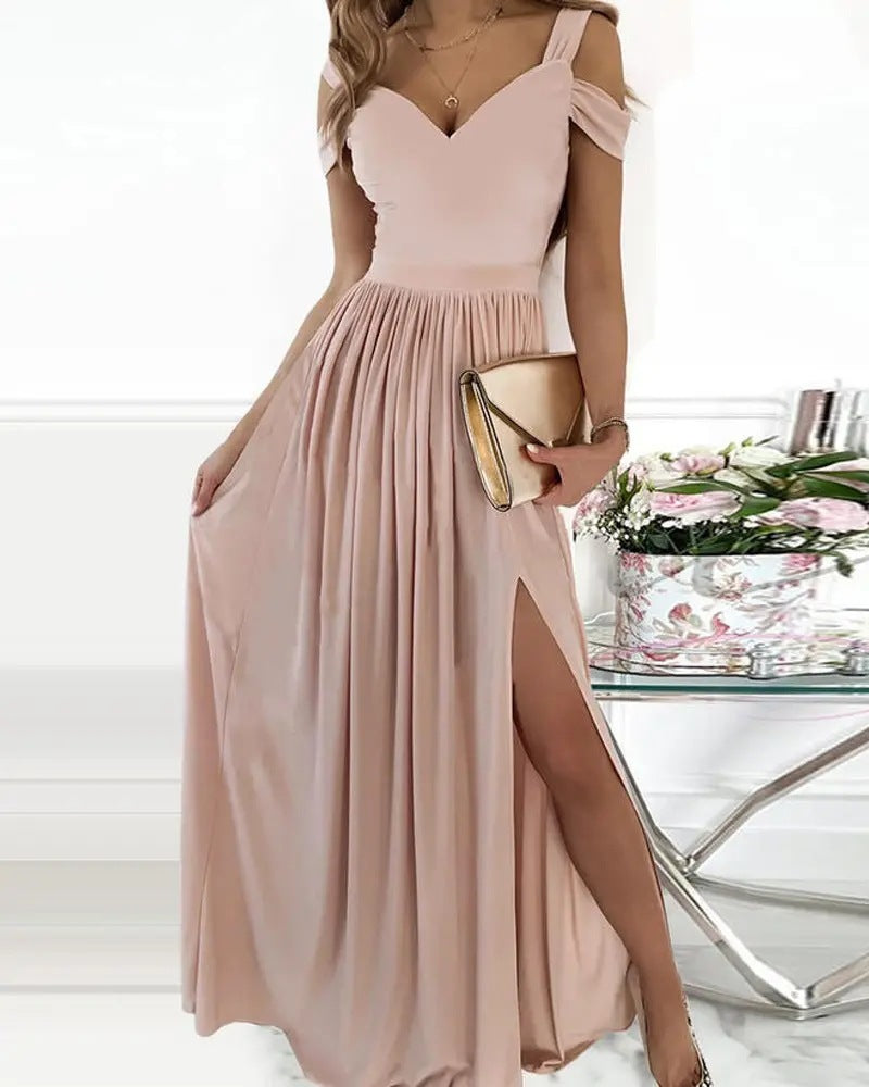 Robe longue rose pâle élégante avec fente, tenue de soirée chic, femme tenant une pochette dorée, décor floral en arrière-plan.