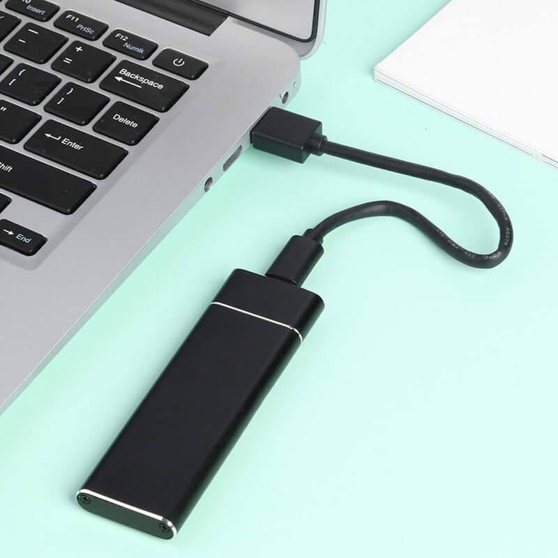 Clé USB noire connectée à un ordinateur portable argenté sur fond vert. Accessoire informatique, stockage de données, technologie portable.