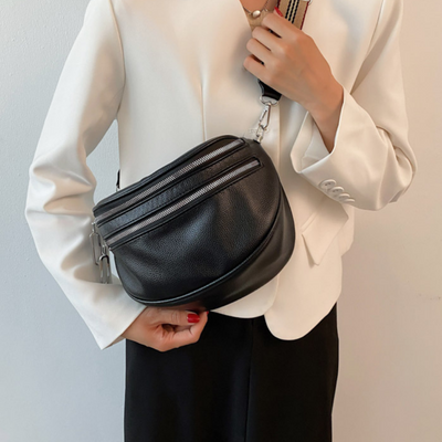 Sac banane en cuir noir porté par une personne en veste blanche. Accessoire mode tendance avec bandoulière ajustable, idéal pour un look chic.