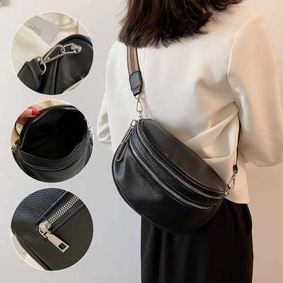 Sac banane en cuir noir porté par une femme, avec bandoulière réglable. Détails des fermetures éclair et compartiments intérieurs visibles. Accessoire mode tendance.