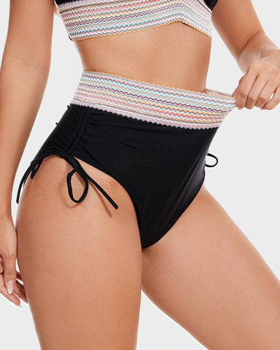 Femme portant un maillot de bain taille haute noir avec détails à rayures colorées et cordons ajustables, mode plage tendance été.
