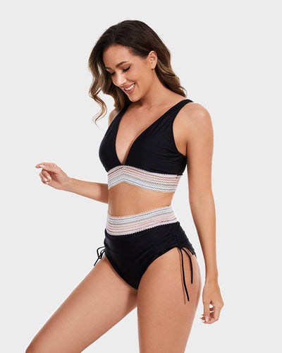 Femme souriante en bikini noir avec détails en crochet coloré, posant de profil sur fond gris. Maillot de bain tendance, mode plage été.