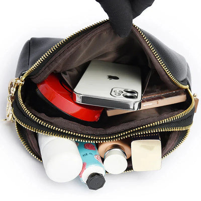 Sac à main noir en cuir ouvert, contenant un smartphone, produits cosmétiques, et accessoires. Organisation pratique, mode, accessoires femme.
