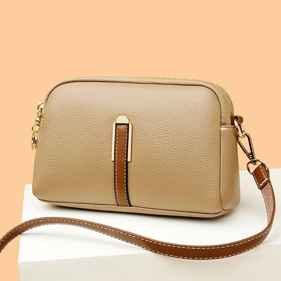 Sac à main en cuir beige élégant avec bandoulière ajustable, fermeture éclair dorée et détails marron, posé sur fond beige. Accessoire mode chic.