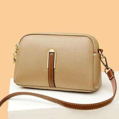 Sac à main en cuir beige élégant avec bandoulière ajustable, fermeture éclair dorée et détails marron, posé sur fond beige. Accessoire mode chic.