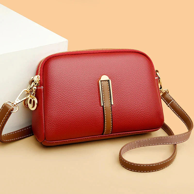 Sac à main en cuir rouge élégant avec bandoulière marron, fermoir doré, posé sur fond beige. Accessoire mode femme tendance et chic.