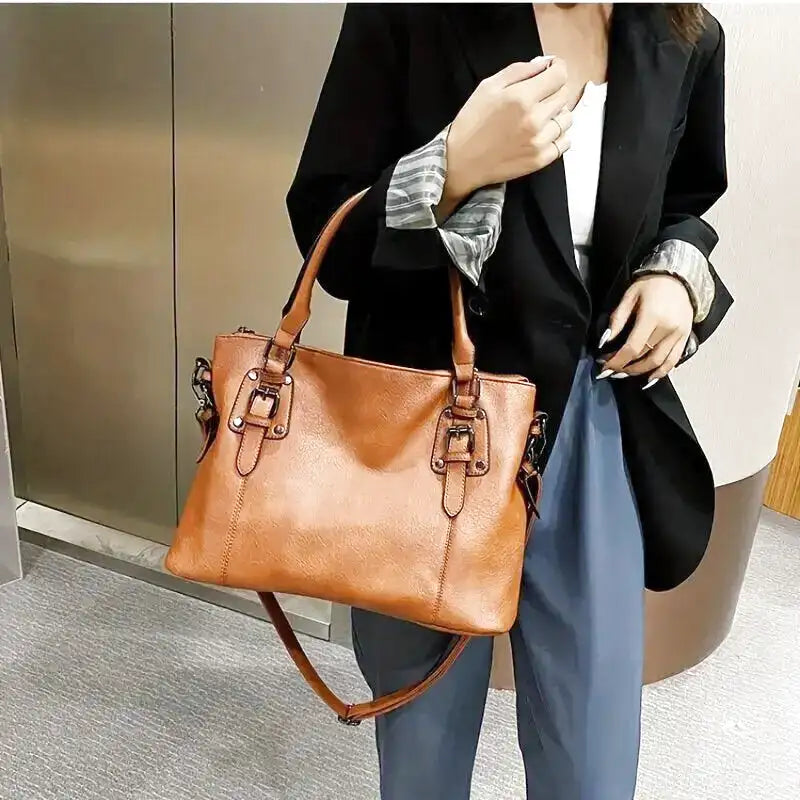 Femme portant un sac à main en cuir marron, tenue élégante avec blazer noir et pantalon bleu, mode urbaine chic, accessoires tendance.