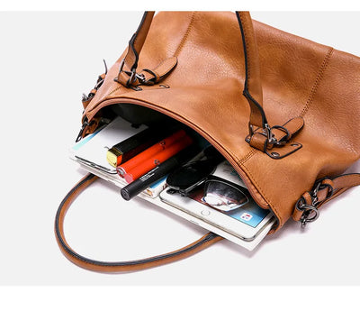 Sac à main en cuir marron ouvert, contenant smartphone, lunettes de soleil, rouge à lèvres et livres. Accessoire mode femme, tendance et pratique.