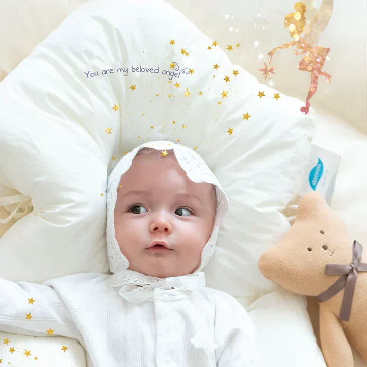 Bébé allongé sur un coussin blanc avec un bonnet, entouré d'étoiles dorées et d'une peluche ours. Texte "You are my beloved angel" visible.