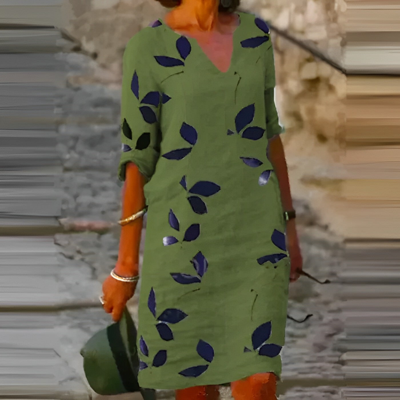 Robe verte à motifs de feuilles bleues, manches retroussées, portée par une femme tenant un chapeau. Mode estivale, style décontracté.