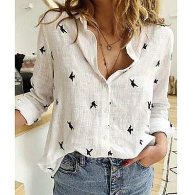 Chemise blanche en lin avec motifs d'oiseaux noirs, manches retroussées, portée par une femme avec un jean décontracté. Mode tendance et élégante.