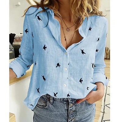 Chemise bleue en lin avec motifs d'oiseaux noirs, manches retroussées, portée par une femme avec un jean taille haute. Mode décontractée chic.