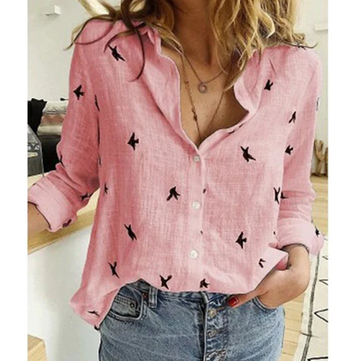 Chemise rose en lin avec motifs d'oiseaux noirs, manches retroussées, portée par une femme. Mode décontractée, tendance, élégance féminine.