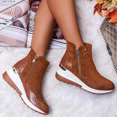 Bottes marron en daim avec fermeture éclair, semelle blanche et détails en cuir croco, posées sur un fond automnal avec magazine et sac à main.