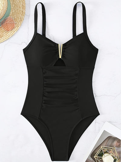Maillot de bain une pièce noir élégant avec détails dorés, design froncé, posé sur fond clair avec chapeau de paille et magazine. Mode plage chic.