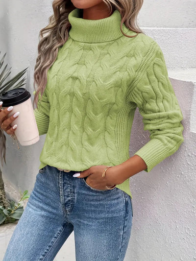 Femme portant un pull vert à col roulé torsadé, tenant un gobelet de café, avec un jean bleu. Mode automne, style décontracté, tendance féminine.