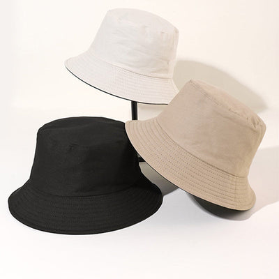 Trois chapeaux bob en coton, couleurs noir, beige et blanc, posés sur fond neutre. Accessoires mode tendance, style décontracté et urbain.