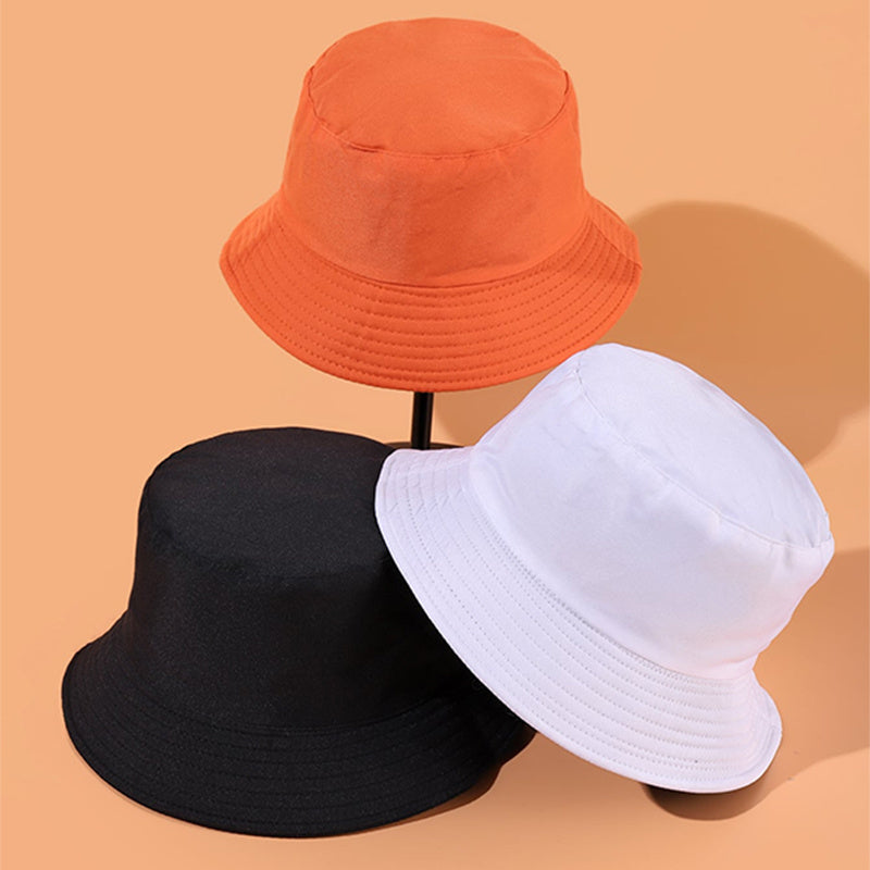 Trois chapeaux bob colorés, orange, noir et blanc, posés sur fond beige. Accessoires de mode tendance, style décontracté, unisexe.