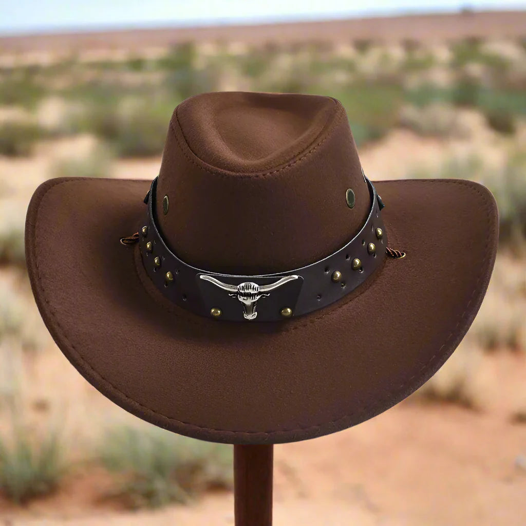 Chapeau de cowboy marron avec bande décorative et motif tête de taureau, posé dans un paysage désertique. Accessoire western authentique.