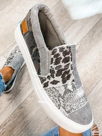 Chaussure slip-on grise et blanche avec motifs léopard et serpent, semelle blanche, sur fond de sol en bois clair. Mode, tendance, chaussures décontractées.