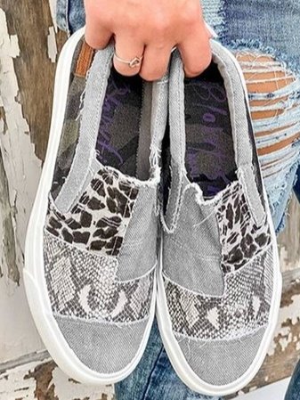 Chaussures en toile grise avec motifs léopard et serpent, tenues par une main. Style décontracté, mode urbaine, jeans déchirés en arrière-plan.