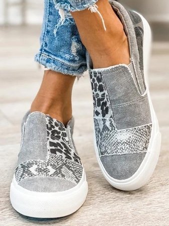 Chaussures slip-on grises pour femme avec motifs léopard et serpent, semelles blanches, portées avec un jean déchiré. Mode décontractée tendance.