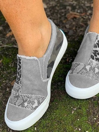Chaussures slip-on grises à motifs camouflage et léopard, semelle blanche, portées sur sol moussu. Sneakers tendance, style décontracté.