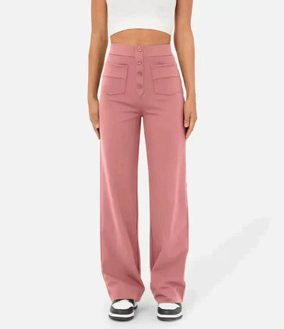 Femme portant un pantalon large rose taille haute avec boutons, poches avant, associé à un haut blanc court et des baskets noires et blanches.
