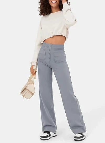 Femme portant un pull blanc court et un pantalon large gris taille haute, tenant un petit sac beige. Mode décontractée, tendance automne.