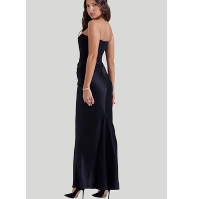 Robe de soirée noire élégante, sans bretelles, portée par une femme, avec des talons noirs et un bracelet doré. Mode féminine chic et sophistiquée.