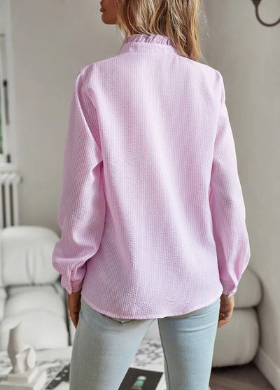 Femme portant une chemise rose texturée, manches longues, dans un salon moderne. Mode féminine, tenue décontractée, style élégant.