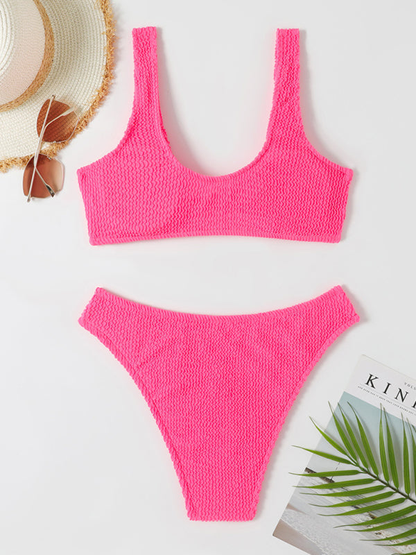 Maillot de bain bikini rose vif texturé sur fond blanc, accompagné de lunettes de soleil, chapeau de paille et magazine, style plage estival.
