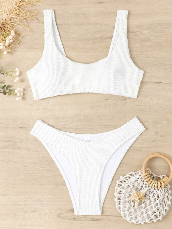 Maillot de bain blanc texturé deux pièces sur fond bois, avec sac en filet et fleurs. Mode plage, été, style tendance, bikini femme.