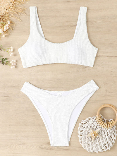 Maillot de bain blanc texturé deux pièces sur fond bois, avec sac en filet et fleurs. Mode plage, été, style tendance, bikini femme.
