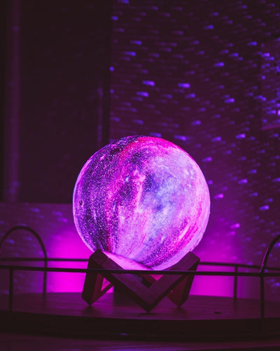 Sphère lumineuse galaxie violette sur support en bois, éclairage LED, effet étoilé, décoration intérieure moderne, ambiance cosmique.