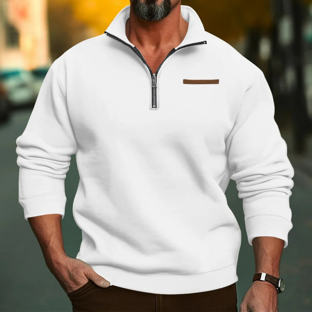 Homme portant un pull blanc à col zippé, manches longues, avec détail marron, en extérieur urbain flou. Mode masculine, style décontracté.