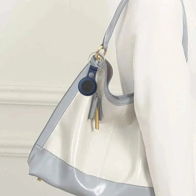 Sac à main en cuir blanc et gris avec porte-clés bleu, porté sur l'épaule. Accessoire mode élégant, tendance, idéal pour un look chic.