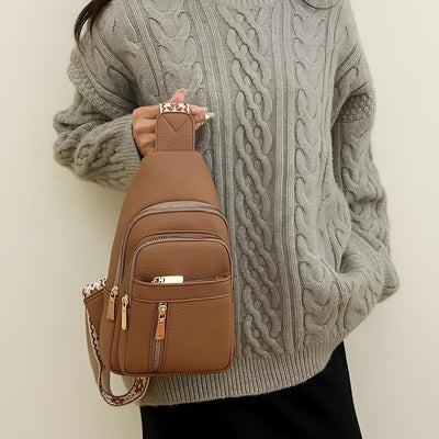 Femme portant un pull en laine torsadée gris avec un sac à dos en cuir marron à bandoulière, mode automne-hiver, accessoires tendance.