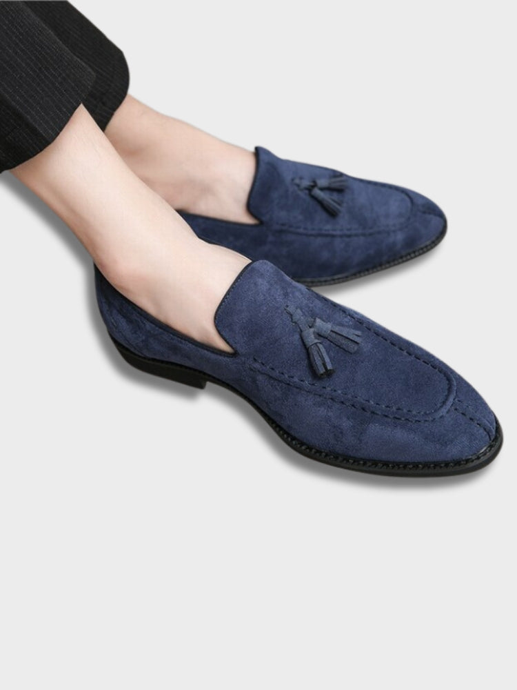 Chaussures mocassins en daim bleu pour homme avec pampilles, élégantes et modernes, portées avec un pantalon noir. Mode masculine chic.