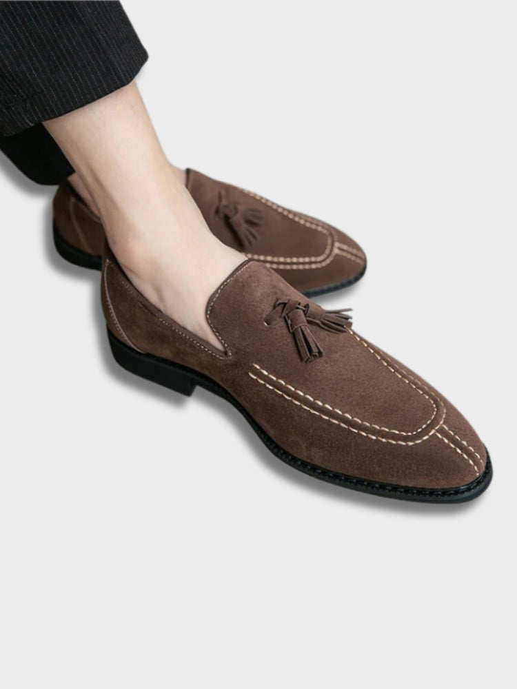 Chaussures mocassins en daim marron pour homme avec pampilles, coutures contrastées, portées avec un pantalon noir. Style élégant et décontracté.