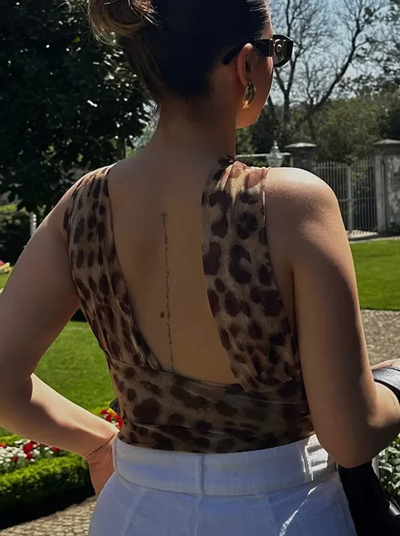 Femme de dos portant un haut à motif léopard, cheveux relevés, lunettes de soleil, dans un jardin ensoleillé. Mode estivale, élégance, plein air.
