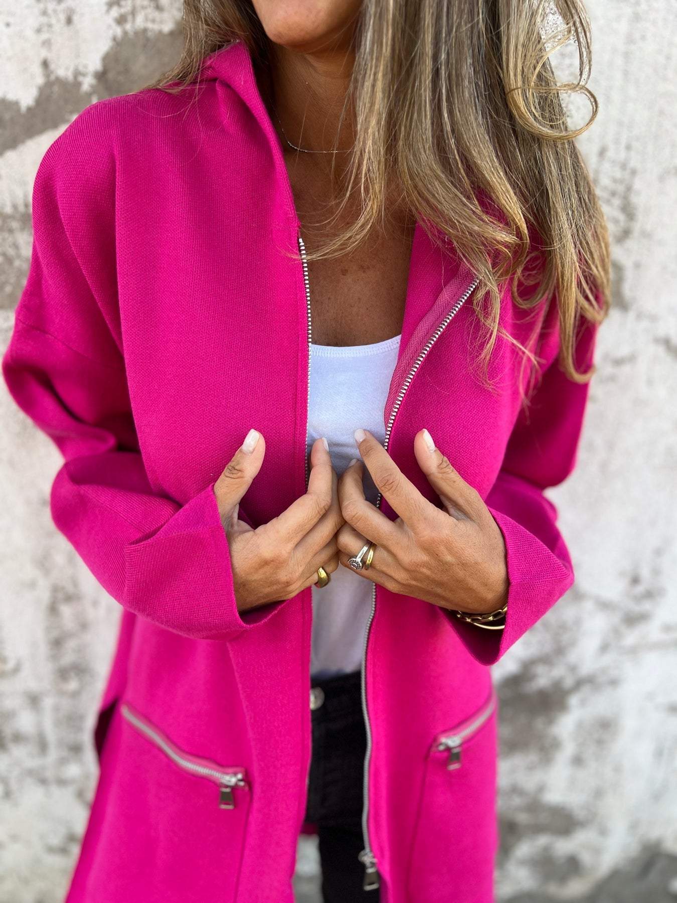Femme portant un manteau rose vif avec fermeture éclair, sur un fond texturé. Mode féminine, style moderne, vêtements tendance automne.