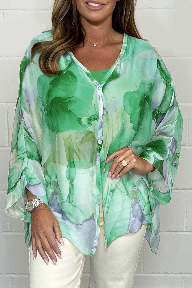 Femme portant une blouse verte fluide à motifs abstraits, manches longues, boutons, sur fond blanc. Mode féminine élégante et tendance.