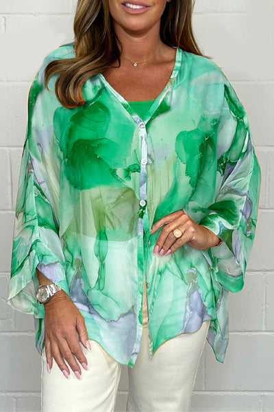 Femme portant une blouse verte fluide à motifs abstraits, manches longues, boutons, sur fond blanc. Mode féminine élégante et tendance.